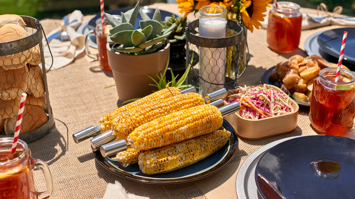 table outdoors with corn on the cob, icetea and a plant